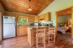 A wooden cabin with a kitchen featuring a refrigerator, microwave, and stove, and a small bar area with stools. - Escape to Naughty by Nature in Gatlinburg: a cozy cabin for two with stunning mountain views. (Gatlinburg)