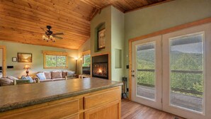 Un intérieur chaleureux avec une cheminée, un plafond en bois et une grande porte-fenêtre coulissante donnant sur l’extérieur.