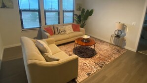 Una sala de estar con un sofá color crema, una mesa redonda de centro y una planta grande.