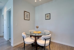 A dining area with a round glass table and four chairs, two framed artworks on the wall, and a wooden floor. - Inviting 2 BR • Near IMG Academy • Pool  (Bradenton)