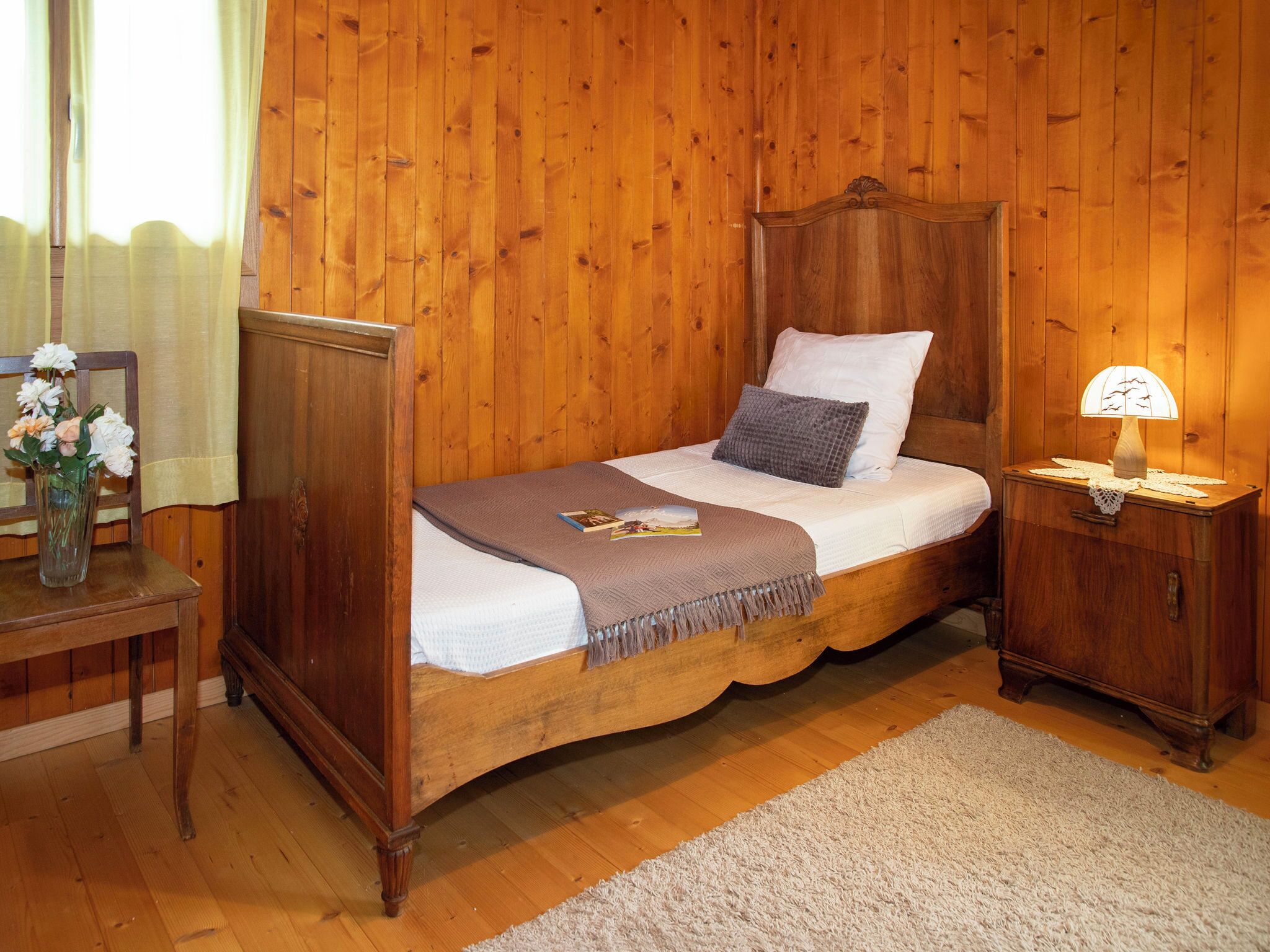 A wooden four-poster bed with a white and gray pillow, a brown throw blanket, and a bedside table with a lamp.