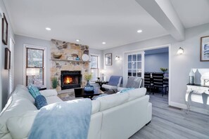Una sala de estar moderna con chimenea de piedra, sofás blancos y un comedor al fondo.