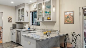 A modern kitchen with white cabinets, a granite countertop, and a built-in island with bar stools. - 3BR Uptown Sedona retreat with red rock views, hot tub, and patio (Sedona)