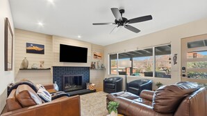A living room with a fireplace, leather sofas, a ceiling fan, and a large TV on the wall. - 3BR Uptown Sedona retreat with red rock views, hot tub, and patio (Sedona)