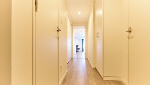 A narrow hallway with wooden flooring and white walls, leading to a room with a chair and a table. - VORT Yamabukicho Residence (Tokyo)