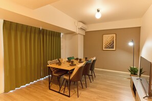 A dining area with a wooden table, chairs, and a green curtain. - VORT Yamabukicho Residence (Tokyo)