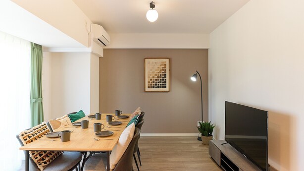 A dining area with a wooden table, chairs, and a flat-screen TV on a stand. - VORT Yamabukicho Residence (Tokyo)
