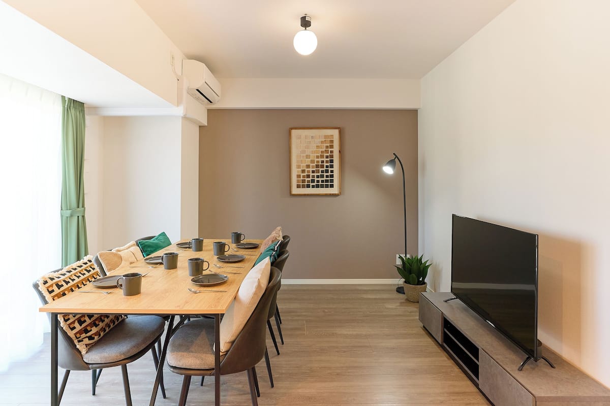 A dining area with a wooden table, chairs, and a flat-screen TV on a stand.