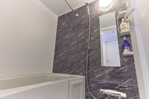 A modern bathroom with a bathtub, a shower, and a marble wall. - VORT Yamabukicho Residence (Tokyo)