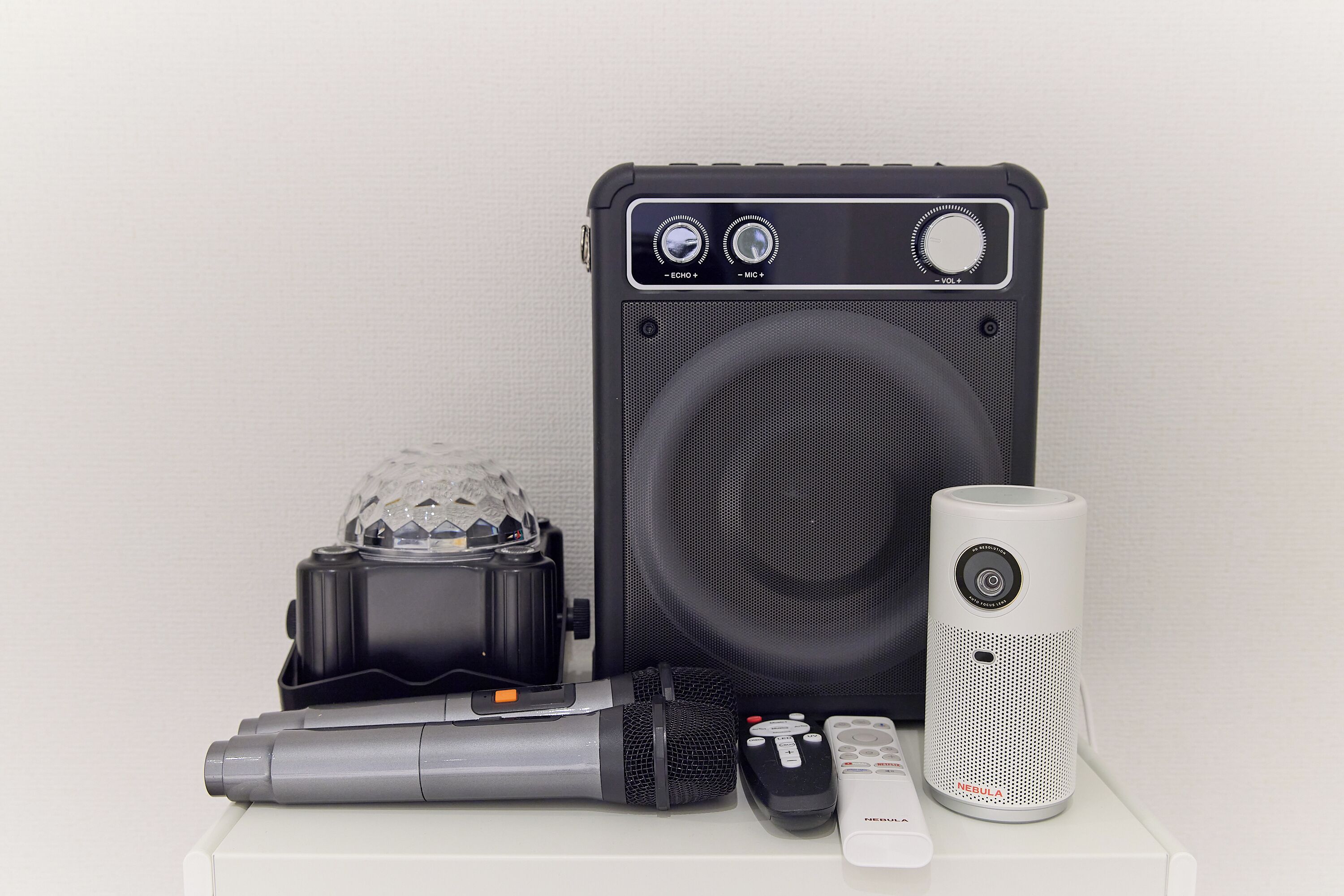 A portable speaker, a microphone, a remote control, and a speaker box with a large speaker and control knobs.