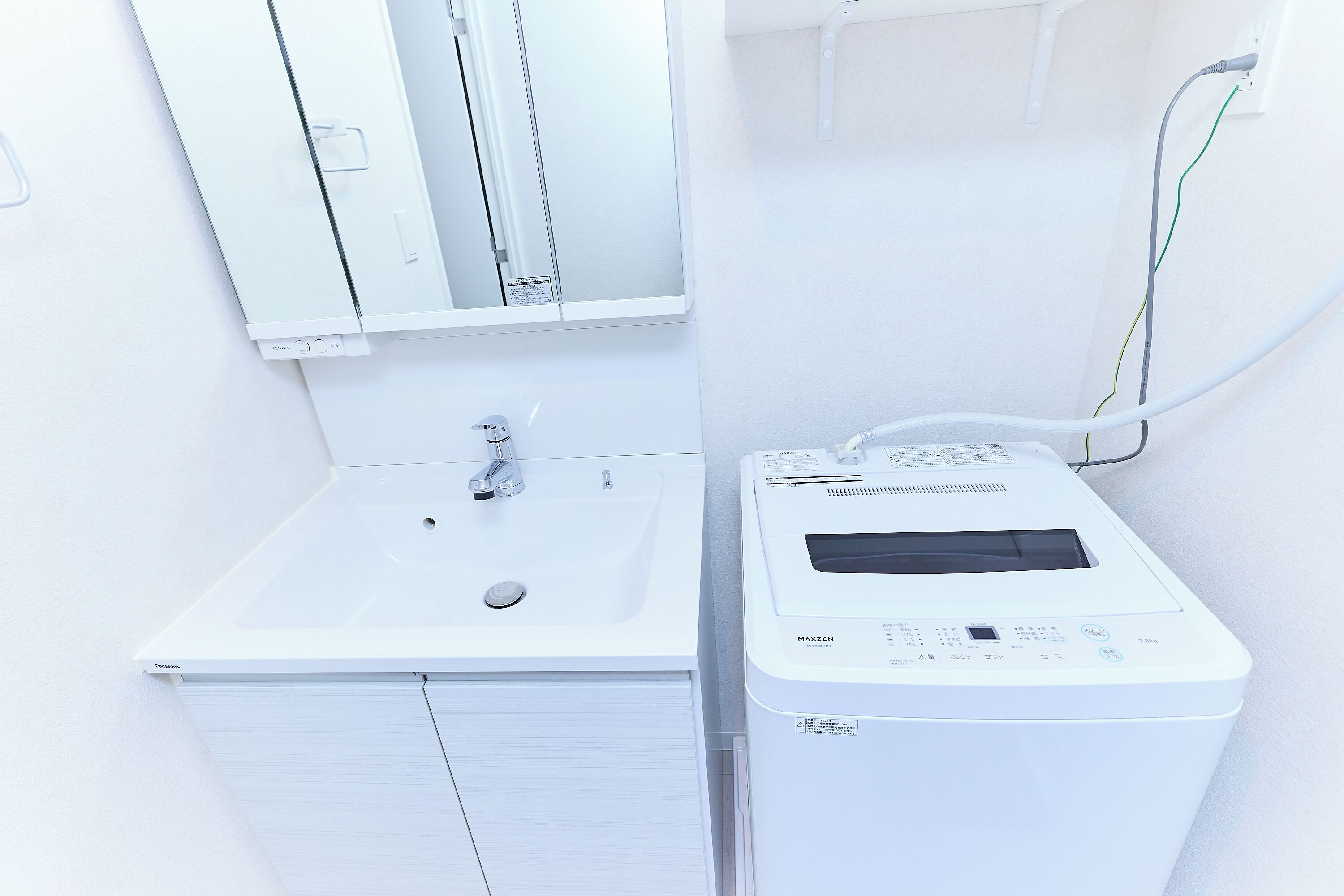 A white bathroom with a sink, mirror, and a white washing machine.