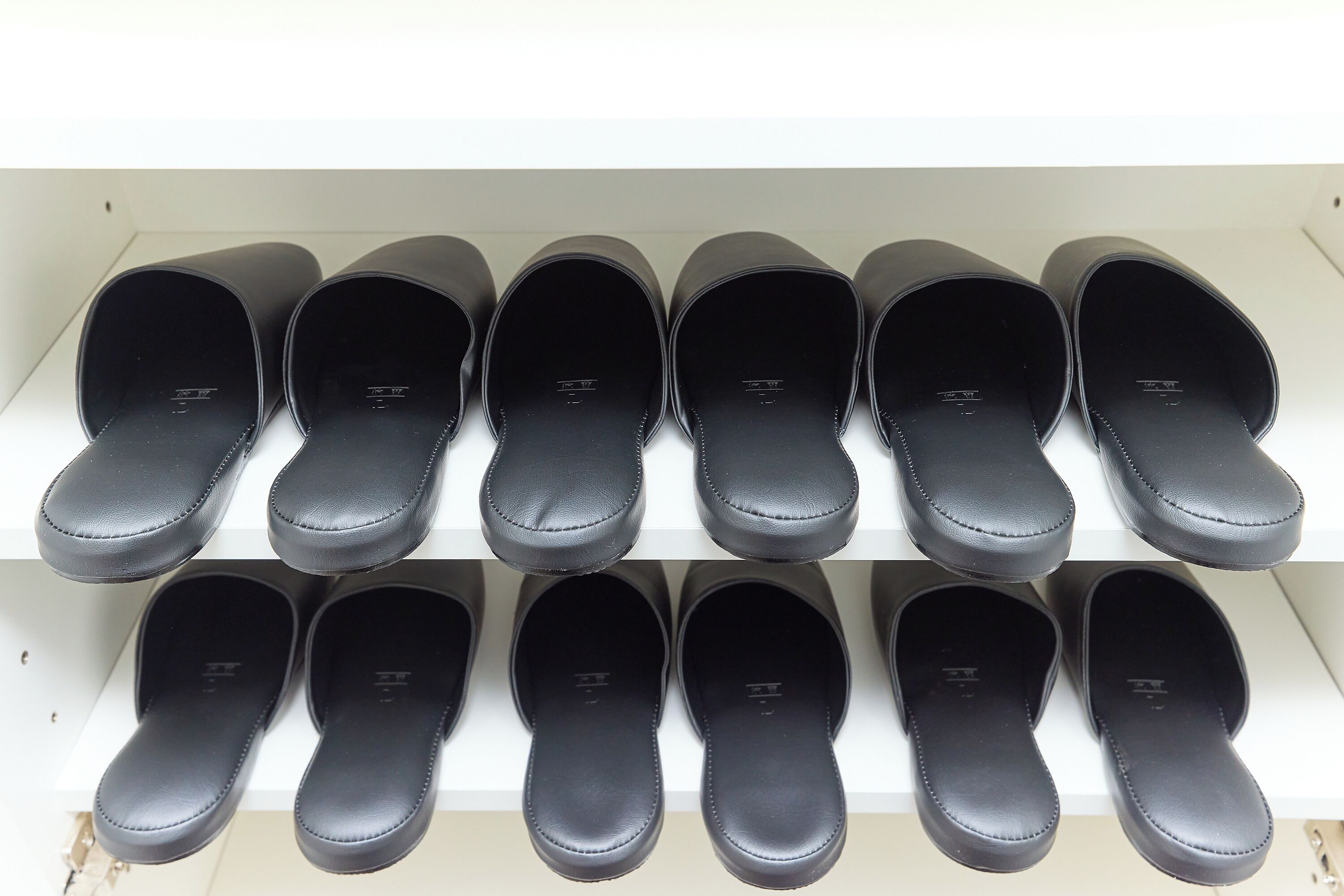 A pair of black slip-on shoes on a white shelf.