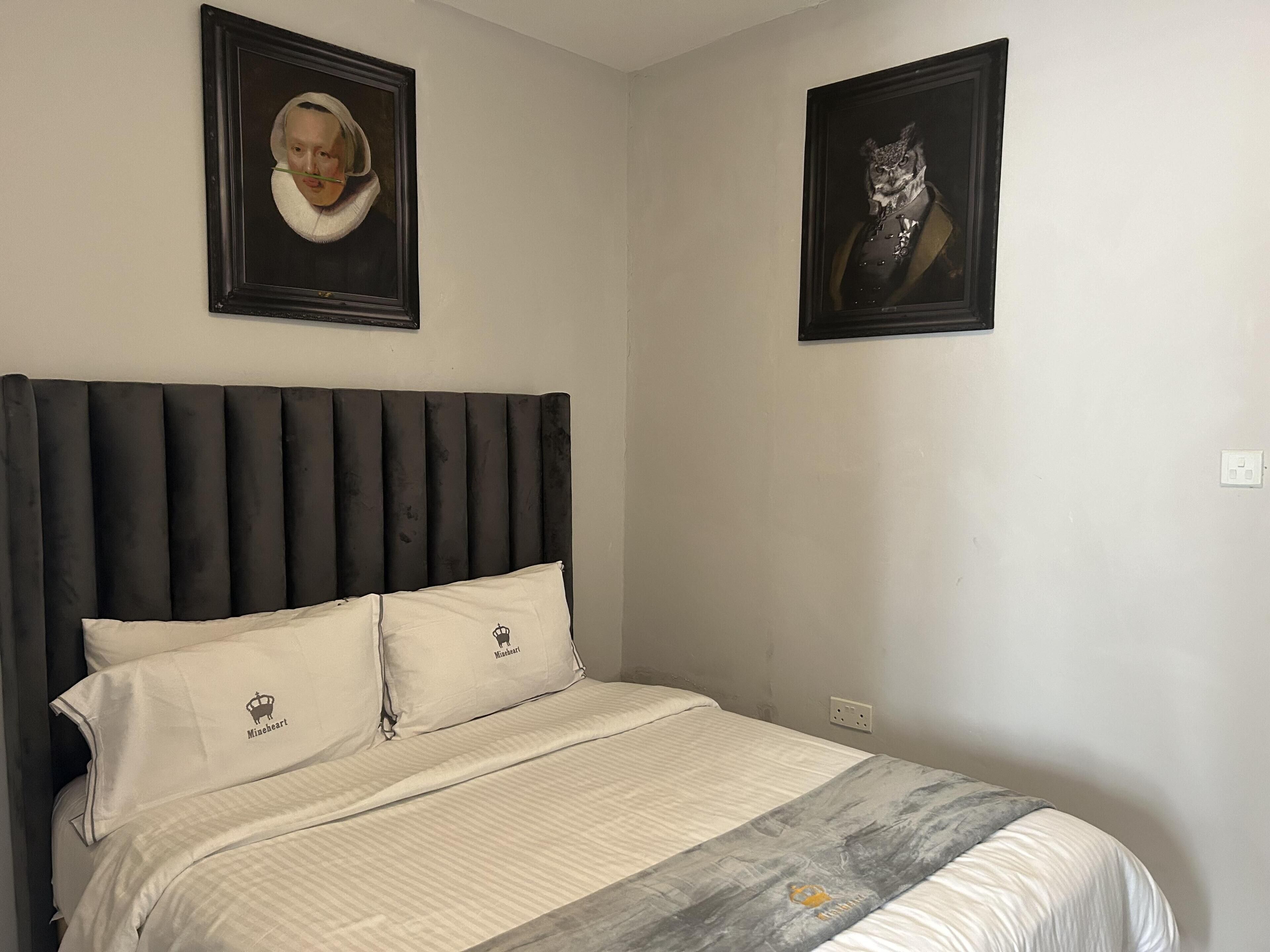 A bedroom with a large bed, two pillows with a logo, a headboard, and two framed pictures on the wall.