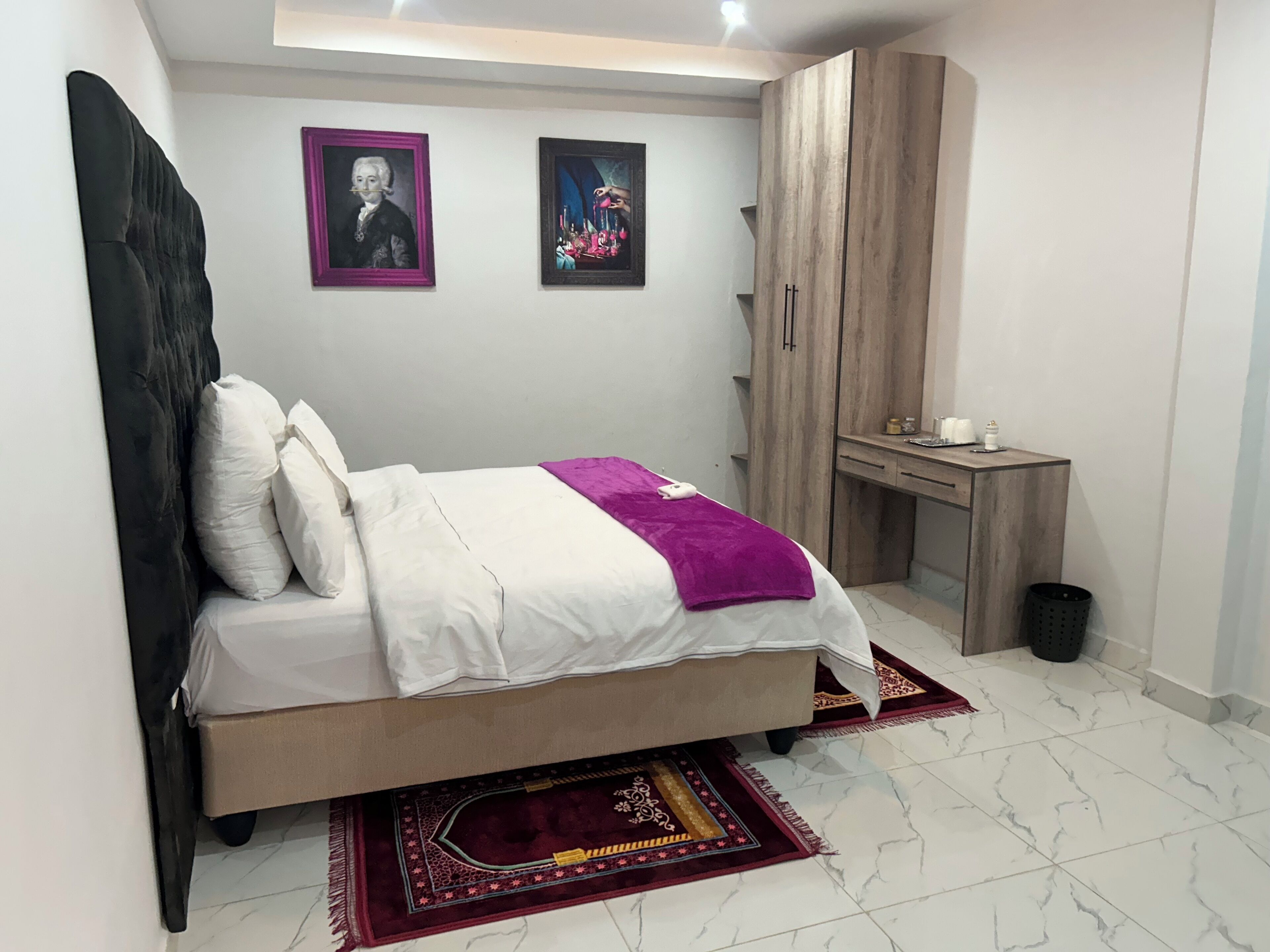 A bedroom with a bed, a desk, and two framed pictures on the wall.