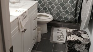 Een badkamer met toilet, wastafel en spiegel. Er is een douchegordijn met een geometrisch patroon.