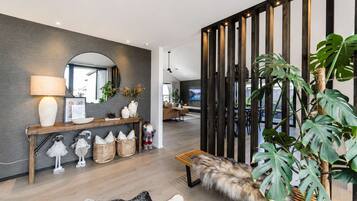 A modern living room with a wooden bench, a console table with decorative items, a large mirror, and a plant.