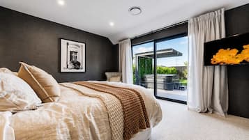 Un dormitorio con una cama grande, un televisor de pantalla plana, un cuadro en la pared y un ventanal corredero que da a un espacio exterior.