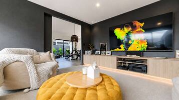 A modern living room with a large flat-screen TV, a round ottoman, and a sofa with a knitted throw.