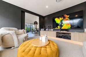 Ein modernes Wohnzimmer mit einem großen Flachbildfernseher, einem runden Hocker und einer Couch mit Strickdecke.