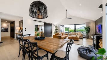 A spacious living area with a wooden dining table, black chairs, a ceiling fan, and a large window offering a view of greenery.