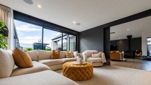 A modern living room with a sectional sofa, ottoman, and a fireplace. - Stylish Home | Private Spa + Indoor & Outdoor Fire (Prebbleton)