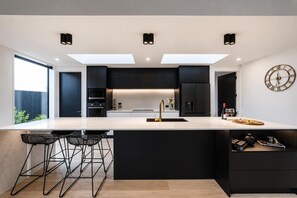 A modern kitchen with a central island, black cabinetry, and a skylight. - Stylish Home | Private Spa + Indoor & Outdoor Fire (Prebbleton)