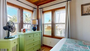 Una habitación con cama, cómoda, ventilador y ventana con cortinas.