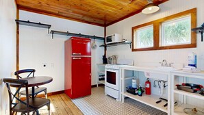 Una cocina compacta con un refrigerador rojo, estufa blanca y pileta blanca. Hay una ventana que proporciona luz natural y un techo de madera.