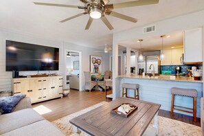 A modern living room with a wooden coffee table, a TV, and a ceiling fan. - Shared Pool, Pet Friendly, Golf Cart Boardwalk to the Beach (Port Aransas)