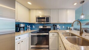Een moderne keuken met witte kasten, roestvrijstalen apparatuur, een blauwe betegelde achterwand en een granieten aanrecht.