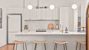 A modern kitchen with white cabinetry, a central island with stools, pendant lighting, and a refrigerator. - The Countess Central Heritage in Launceston (Launceston)