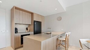 Una cocina moderna con una isla central, armarios de madera, un refrigerador negro y una zona de comedor con sillas blancas.