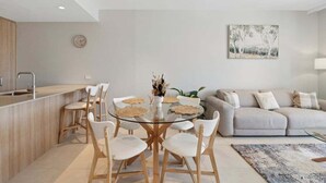 Una cocina moderna con una mesa de comedor de vidrio, sillas blancas y un sofá gris.