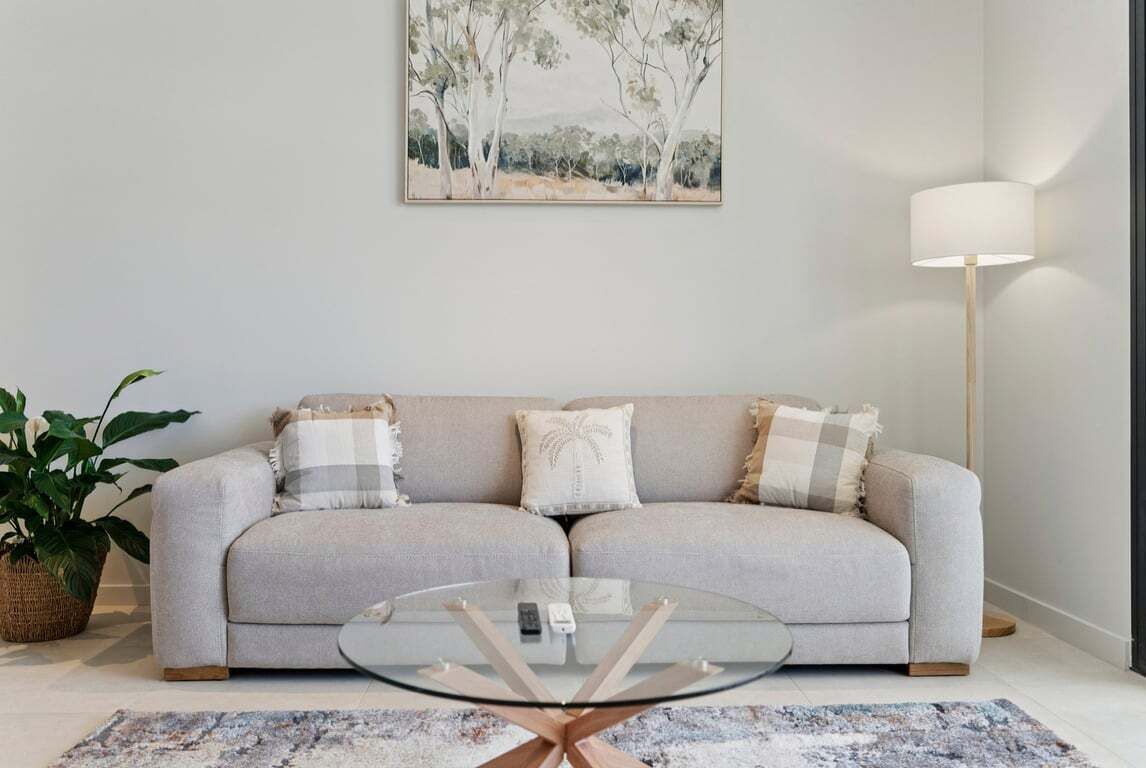 A living room with a sofa, a glass coffee table, a lamp, and a painting on the wall.
