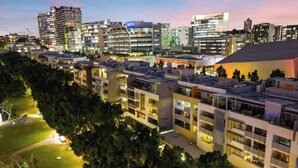 Et moderne hotelkompleks med flere bygninger, en veloplyst gårdhave og en bysilhuet i baggrunden.