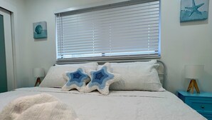 Ein Schlafzimmer mit einem Bett, einem Fenster mit Jalousien, einem Nachttisch und einer Wand mit einer Meerstern-Dekoration.