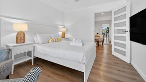 A modern hotel room with a large bed, white walls, wooden flooring, a ceiling fan, and a TV. - Garigal Studio with Pool Access and EV charger (Forestville)