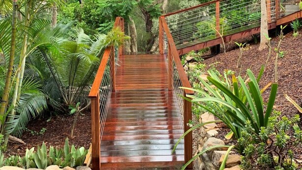 A wooden staircase leading to a covered area surrounded by lush greenery and rocks. - Garigal Studio with Pool Access and EV charger (Forestville)