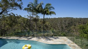A swimming pool with a clear view of the surrounding forest and a palm tree. - Garigal Studio with Pool Access and EV charger (Forestville)