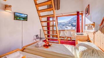 Ein Zimmer mit einem Bett, einem Schreibtisch, einem Sessel, einem Fernseher und einem Fenster mit Bergblick.
