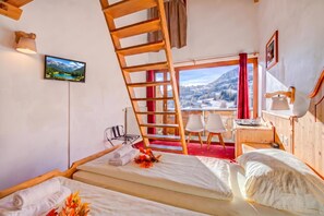 Une chambre avec un lit, un bureau, une chaise, une télévision et une fenêtre donnant sur les montagnes.