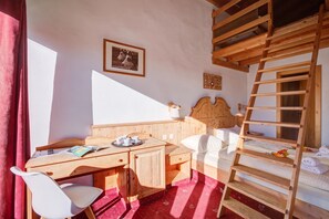 Een kamer met een houten bureau, een bed met een houten hoofdeinde, een ladder en een lijst met een afbeelding aan de muur.