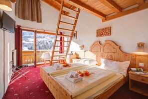 Habitación de hotel con techo de madera, cama con ropa de cama blanca, cabecero de madera, mesita de noche, lámpara y ventana con vistas a un paisaje nevado, además de una alfombra roja.