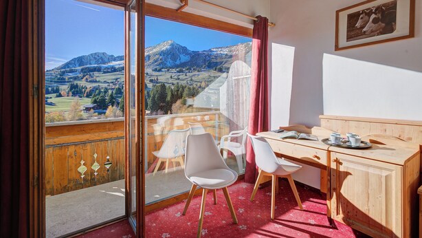 Une chambre avec balcon, un bureau avec des chaises et une vue sur les montagnes.
