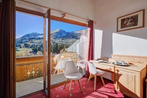 Une chambre avec balcon, un bureau avec des chaises et une vue sur les montagnes.