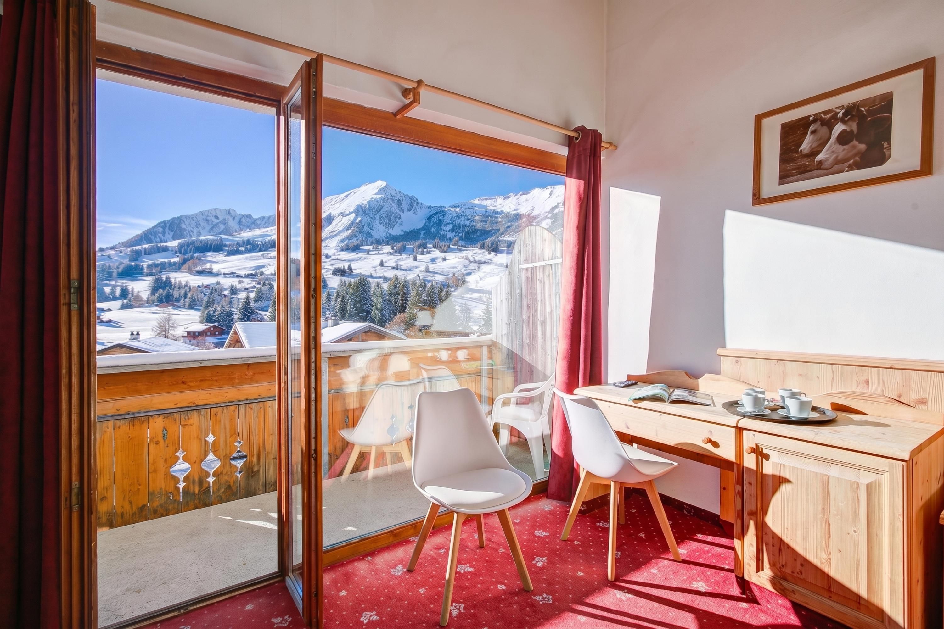 Ein Zimmer mit einem Holztisch, zwei Stühlen, einem Esstisch und Blick auf schneebedeckte Berge.