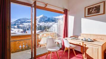 Ein Zimmer mit einem Holztisch, zwei Stühlen, einem Esstisch und Blick auf schneebedeckte Berge.