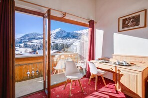 Een kamer met een houten bureau, twee stoelen, een eettafel en uitzicht op met sneeuw bedekte bergen.