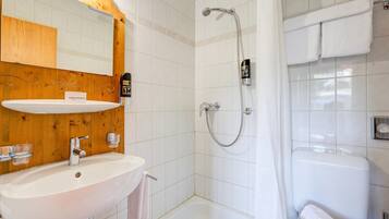Ein Badezimmer mit einem Holz-Waschtisch, einem weißen Waschbecken, einem Spiegel, einer Dusche mit Duschbrause und einer weißen Badewanne.