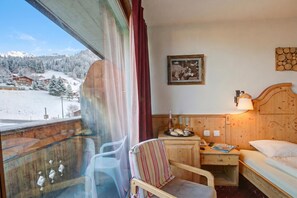 Habitación de hotel con cama, una silla, una mesita con lámpara, un cuadro en la pared y vista a un paisaje nevado a través de una ventana.